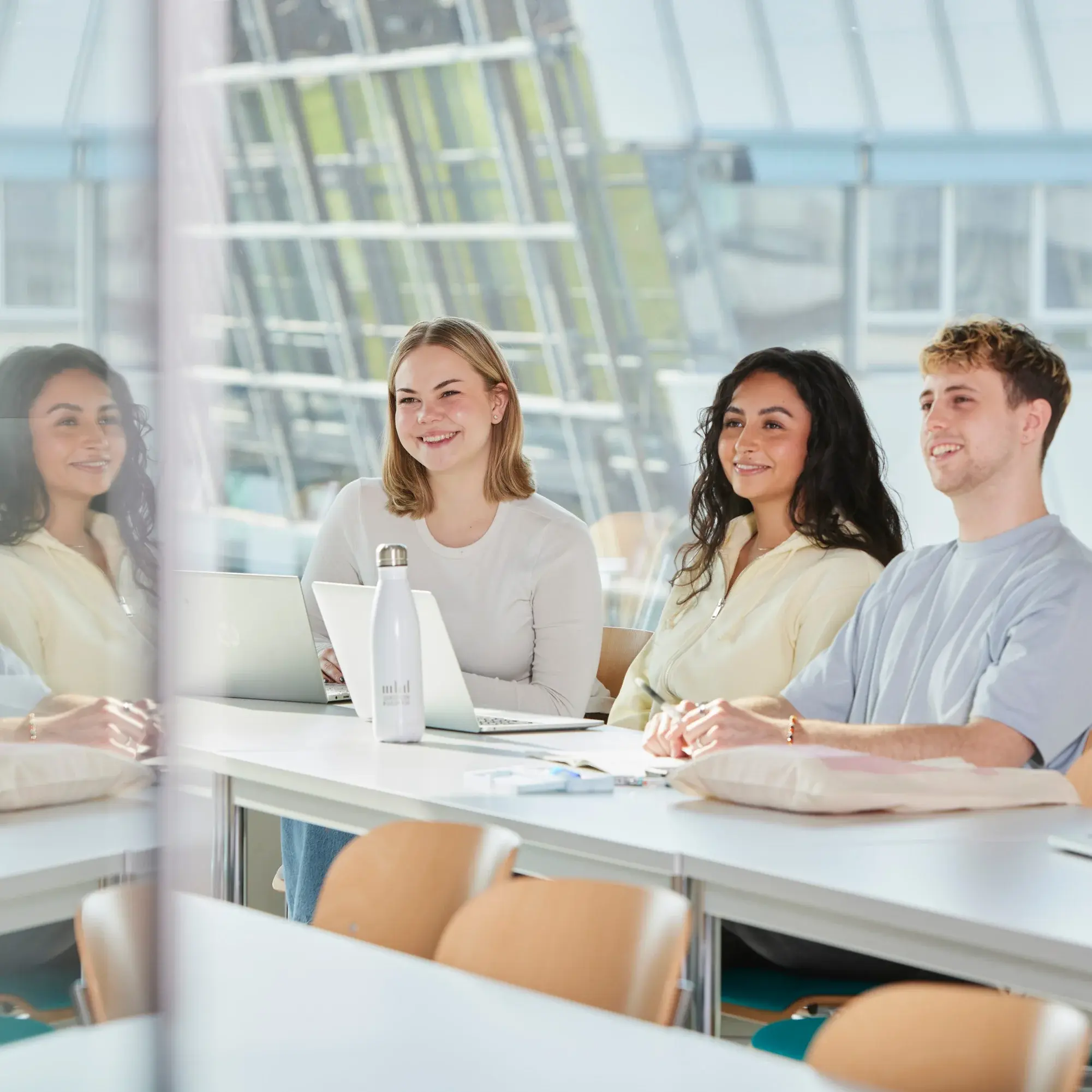 Drei Studierende sitzen in einem hellen Vorlesungsraum und arbeiten.
